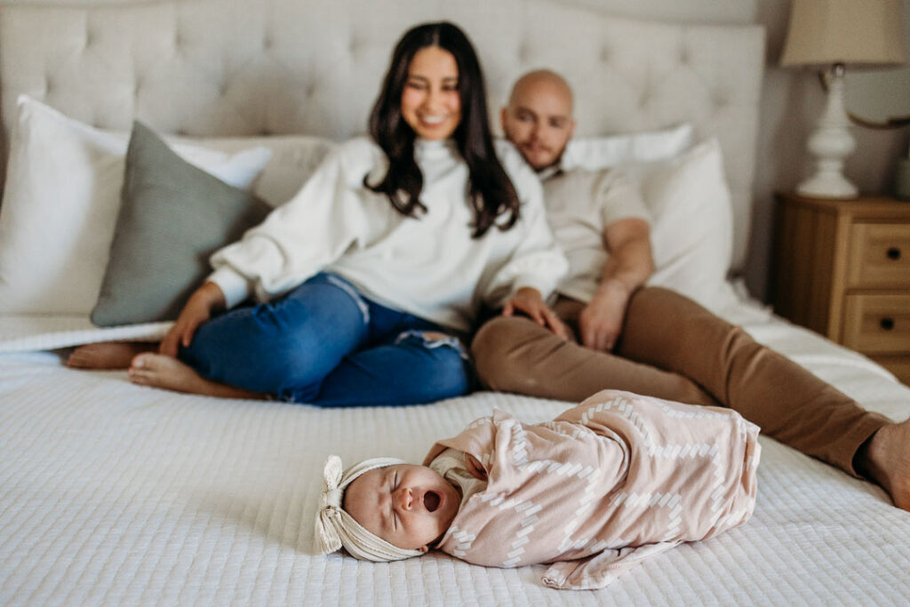 Mom and Dad with newborn baby girl in-home cuddled up on their bed 